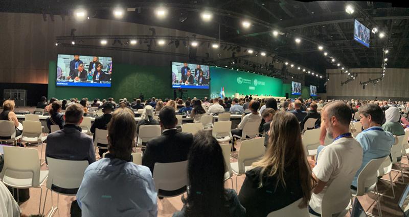 Audience members watching a presentation in a large auditorium at COP28