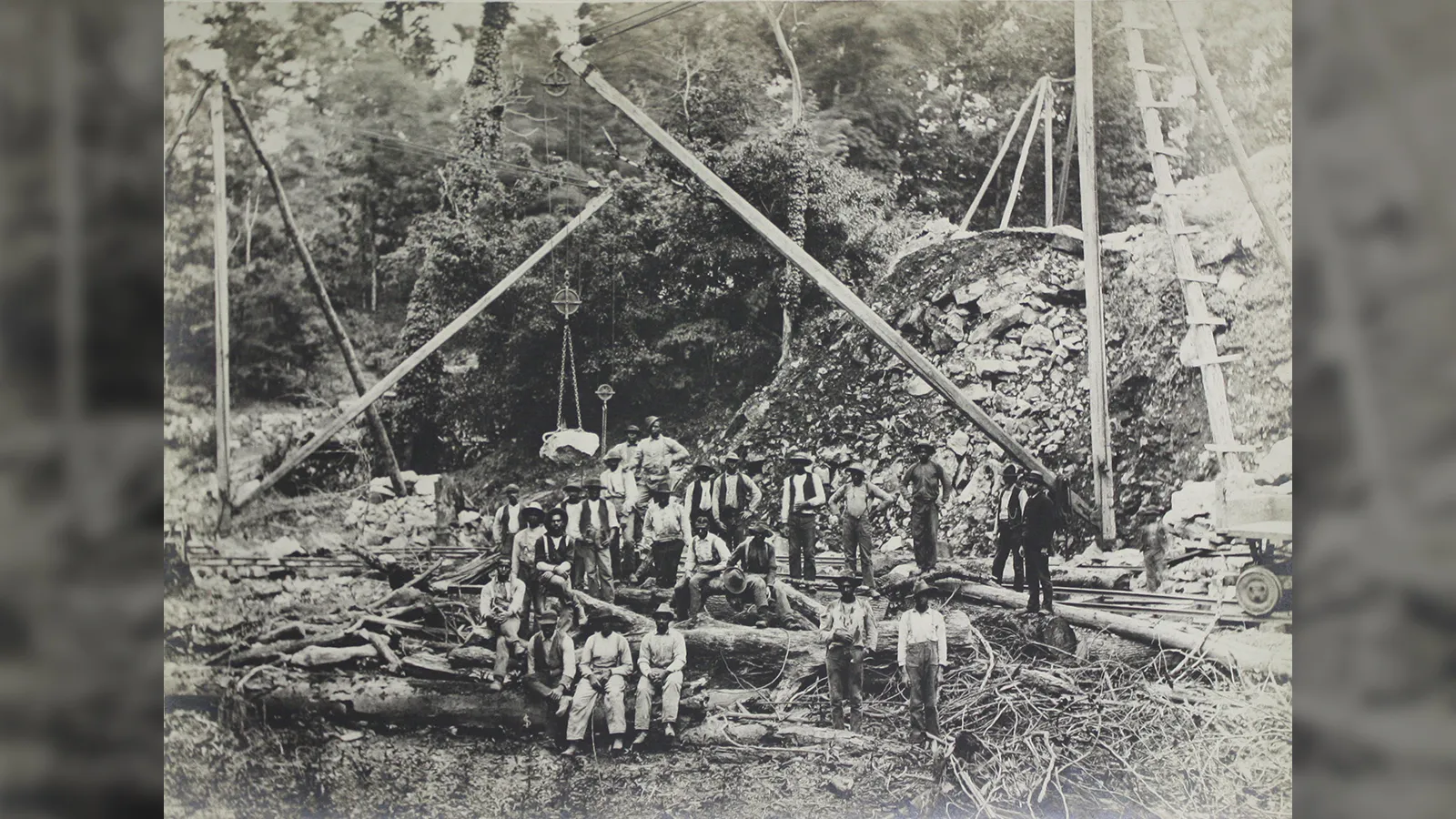 Laborers posing at a heavy construction or quarry site utilizing a large wooden derrick crane system