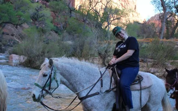 Student on horseback riding through a stream