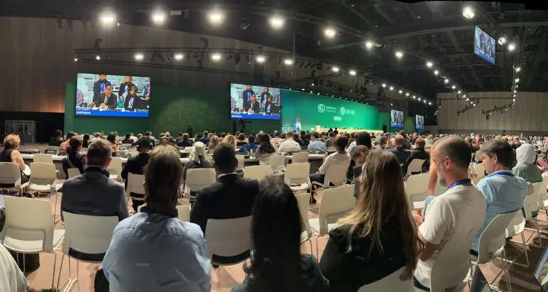 Audience members watching a presentation in a large auditorium at COP28