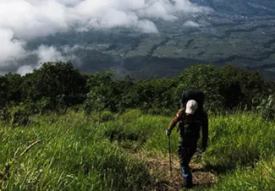Hiker climbing a mountain with clouds and fields far below him