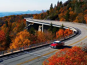 Red car driving on acurving bridge over a forested mountainside