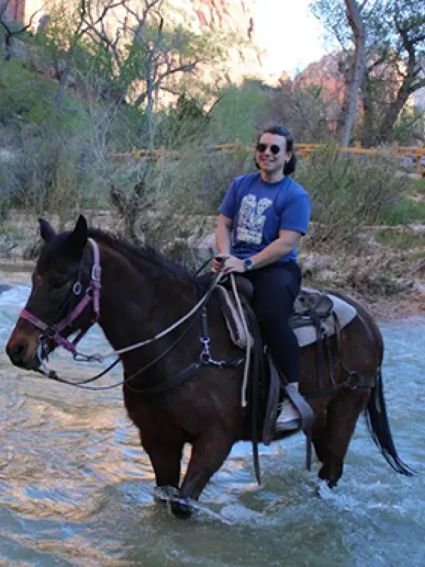 Woman riding a horse through a stream in a canyon